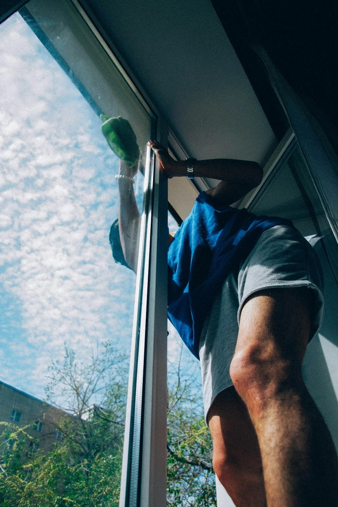 Close-up of hand cleaning window with squeegee outdoors using yellow gloves.